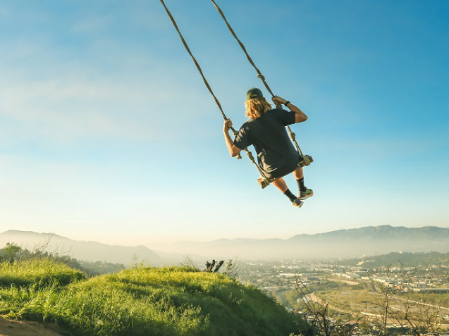 Jugendliche sitzt auf einer Schaukel, die hoch über die hüglige Landschaft fliegt