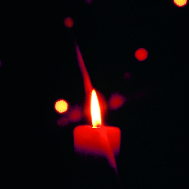 Eine einzelne rote Kerze brennt hell in der Dunkelheit, umgeben von kleinen, leuchtenden roten und weißen Bokeh-Lichtern, die im schwarzen Hintergrund verstreut sind.