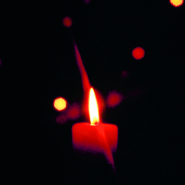 Eine einzelne rote Kerze brennt hell in der Dunkelheit, umgeben von kleinen, leuchtenden roten und weißen Bokeh-Lichtern, die im schwarzen Hintergrund verstreut sind.